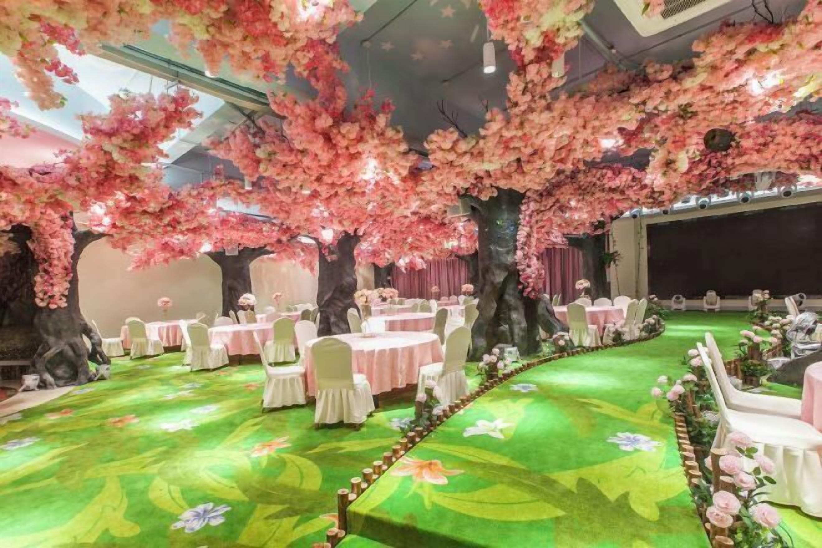A banquet hall with round tables, white chairs, and a green floral carpet.