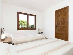 Quarto com duas camas, uma janela, porta de madeira e uma cadeira com sapatos.