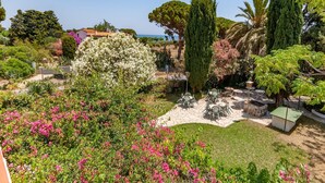 Un jardín con diversas plantas y flores, mobiliario exterior y vista al mar.