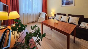 Ein helles Wohnzimmer mit einem Couchtisch aus Holz, einer Couch mit gemusterten Kissen, einem Sessel und einer Lampe.