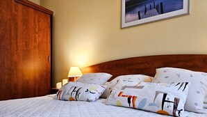 Ein ordentlich bezogenes Bett mit gemusterten Kissen, einer Nachttischlampe und einem gerahmten Bild an der Wand.