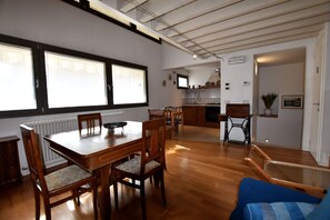 Un'ampia zona pranzo con tavolo e sedie in legno, una cucina sullo sfondo e vista sulla città attraverso ampie finestre.
