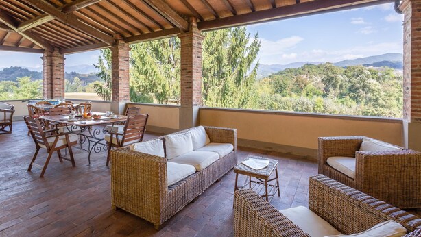 A covered outdoor seating area with wicker furniture and a table, overlooking a scenic landscape. - Villa in Mugello Hills with Private Pool (Vicchio)