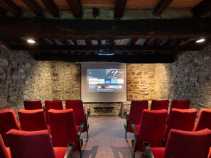 Cine con paredes de piedra, asientos de terciopelo rojo y una pantalla que muestra servicios de streaming.