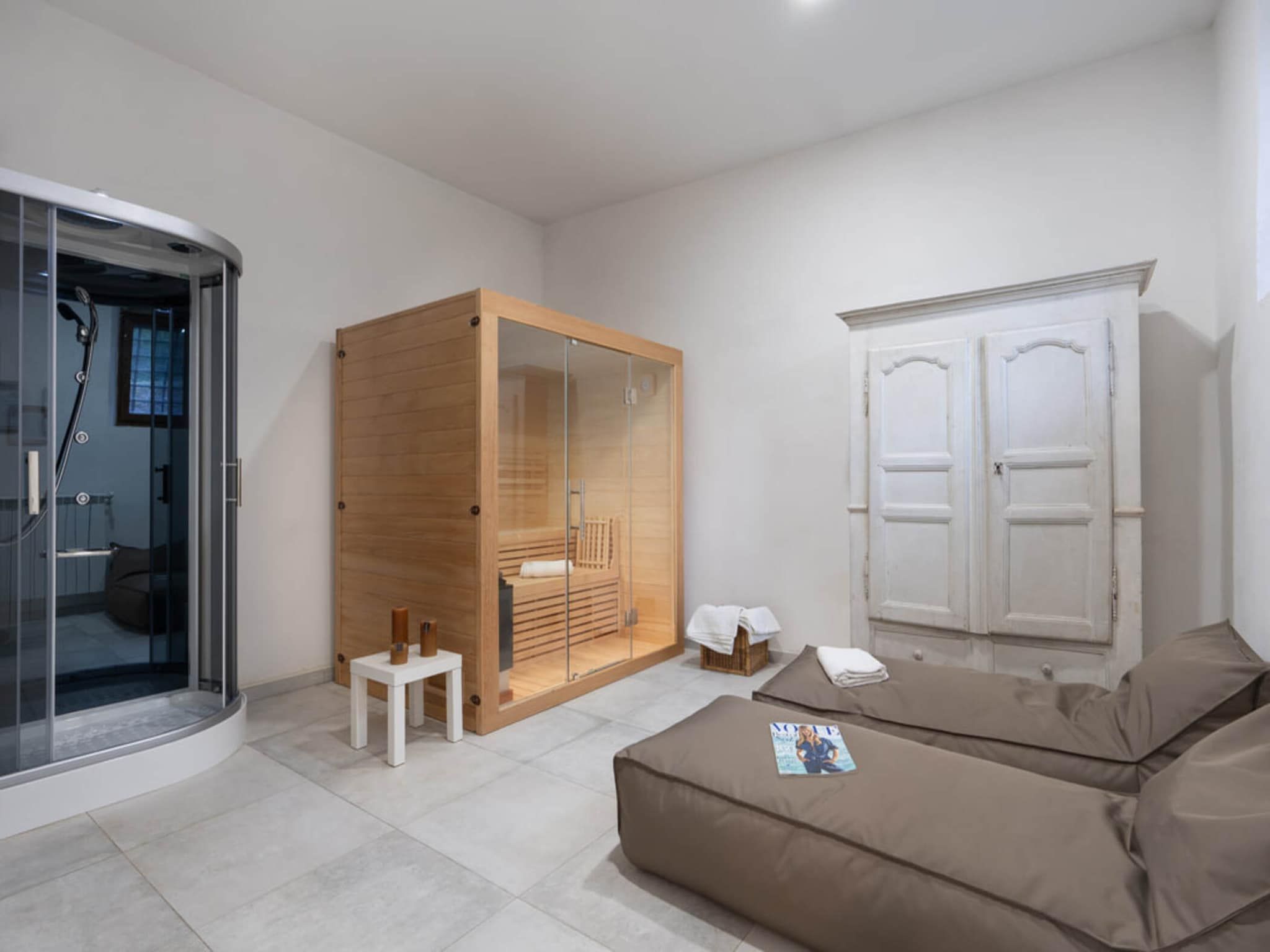 A modern bathroom with a glass shower enclosure, a wooden wardrobe, a white cabinet, and a beige sofa.