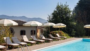 A poolside area with lounge chairs and umbrellas, a clear sky, and mountains in the background. - Villa in Mugello Hills with Private Pool (Vicchio)