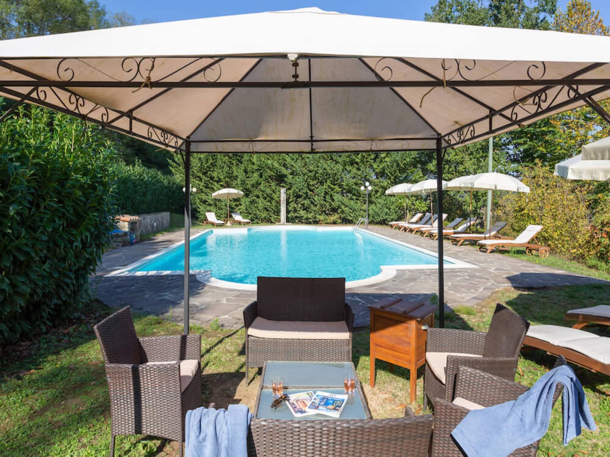 A covered outdoor seating area with a pool, surrounded by greenery.
