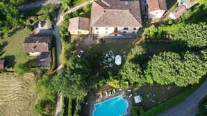 An aerial view of a residential area with a swimming pool surrounded by greenery, a road, and houses with tiled roofs. - Villa in Mugello Hills with Private Pool (Vicchio)
