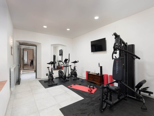 A gym with various exercise equipment, a television, and a red mat.