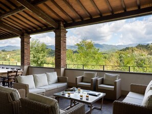 Un área de estar al aire libre con mobiliario de mimbre y una mesa, con vistas a un paisaje montañoso.