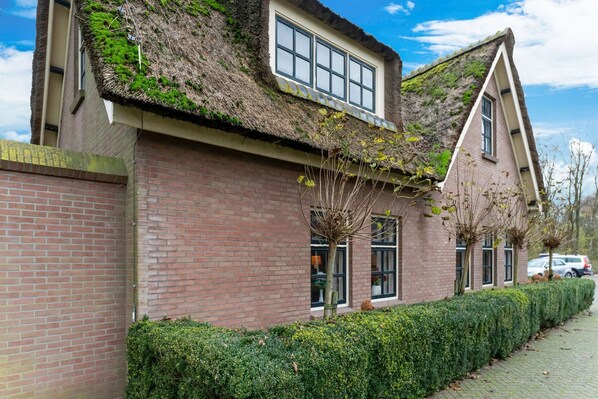 A traditional brick building with a thatched roof and a window with a white frame.
