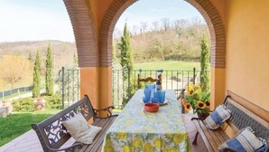 An outdoor patio with a table set for two, benches, and a view of a grassy area with trees.