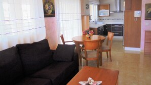 Una sala de estar con un sofá, una mesa de comedor con sillas, una zona de cocina con armarios y una estufa, y un cuadro en la pared.