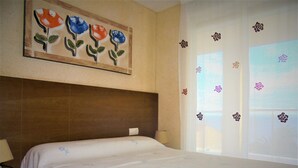Habitación de hotel con cama, mesita de noche, lámpara, un cuadro de flores y una ventana con cortinas florales.