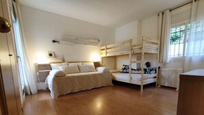 A room with a bunk bed, a single bed, a bedside table, a lamp, and a window with curtains. - Apto Residencial en Tamariu with Mountain View, Pool, Wi-Fi & Garden (Tamariu)