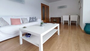 A minimalist living room with a white sofa, a coffee table, and a dining area with a white table and chairs. - Apto Residencial en Tamariu with Mountain View, Pool, Wi-Fi & Garden (Tamariu)