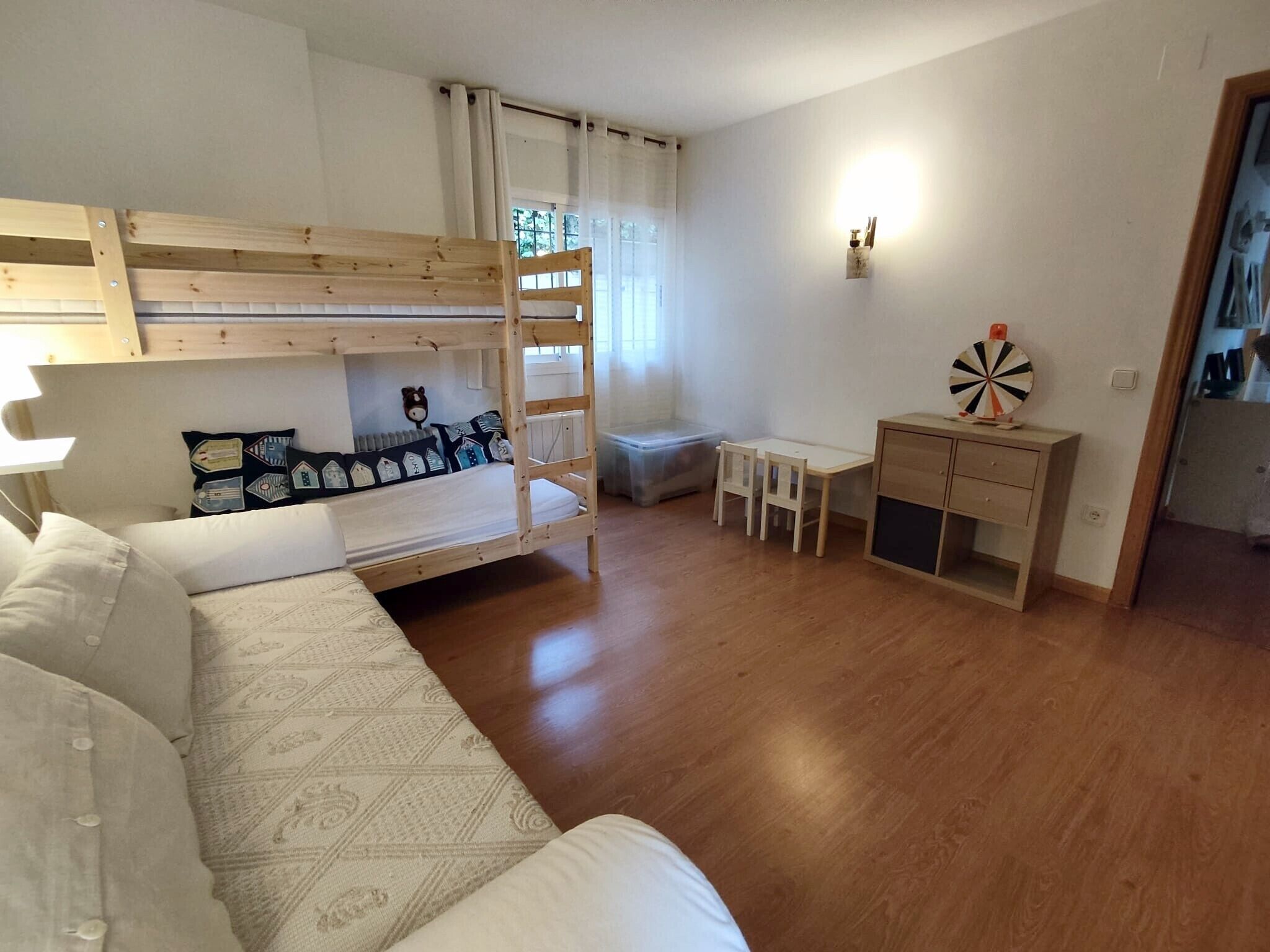 A bunk bed with a ladder, a small desk with a chair, a white sofa, and a window with curtains.
