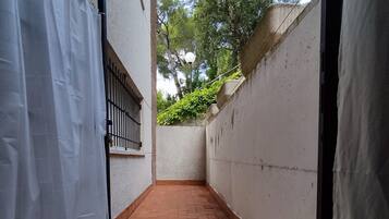 Un estrecho sendero de ladrillo que conduce a una entrada protegida por una cortina blanca, un portón de metal y un muro blanco con un pequeño ventanal.