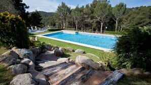 A rectangular swimming pool surrounded by a well-maintained lawn, with large rocks and a wooden deck leading to the pool. - Apto Residencial en Tamariu with Mountain View, Pool, Wi-Fi & Garden (Tamariu)