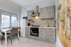 Une cuisine moderne avec des meubles gris, un four encastré et un coin repas comprenant une table et des chaises blanches.