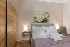 A neatly made bed with white linens and pillows, a bedside table with a lamp, a painting of flowers on the wall, and a wooden wardrobe. - Studio Apartment "Riverview 67 1" with Garden & Wi-Fi (Salionze)