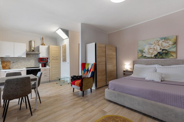 A modern hotel room with a bed, a dining area, a kitchen, and a bathroom.