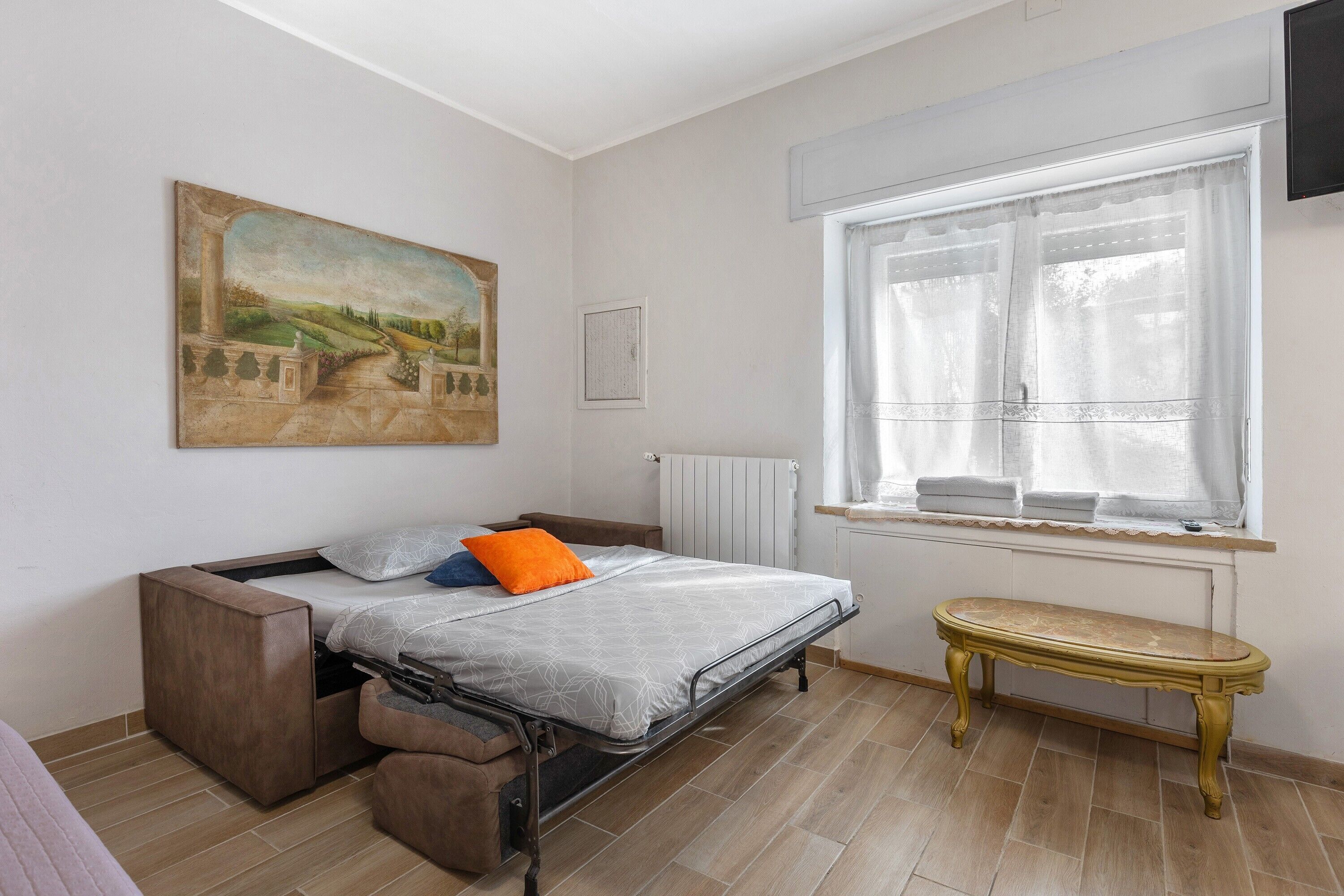 A bedroom with a bed, a bench, a radiator, a window, and a painting on the wall.