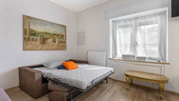 A bedroom with a bed, a bench, a radiator, a window, and a painting on the wall.