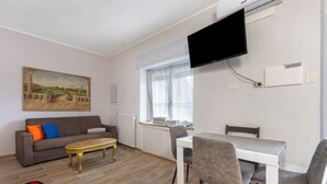 Ein Wohnzimmer mit einer Couch, einem Couchtisch, einem an der Wand befestigten Fernseher und einem Fenster mit Vorhängen.