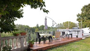 Eine Terrasse im Freien mit Tisch und Stühlen, Blumentöpfen und einem Geländer mit Blick auf einen Garten.