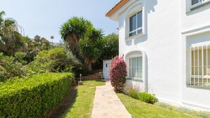 A white building with a stone pathway leading to the entrance, surrounded by well-maintained greenery and a clear sky. - Bright and Cosy Apartment with Sea Views, Shared Pool and Wi-Fi (Mijas Costa)