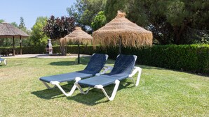 A garden with two lounge chairs and thatched umbrellas, surrounded by greenery and trees. - Bright and Cosy Apartment with Sea Views, Shared Pool and Wi-Fi (Mijas Costa)
