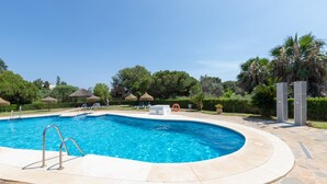 A swimming pool with a stone deck, surrounded by greenery and a clear sky. - Bright and Cosy Apartment with Sea Views, Shared Pool and Wi-Fi (Mijas Costa)