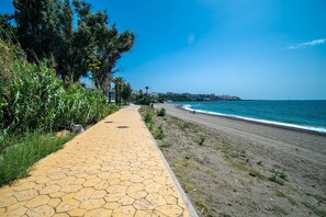 A paved walkway beside a beach with a clear view of the ocean and distant buildings.