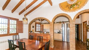 Un comedor con una mesa y sillas de madera, una cocina con refrigerador y un ventilador decorativo.