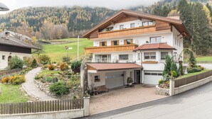 A multi-story building with a garage, surrounded by a landscaped garden and a wooden fence. - Apartment "Pramstaller Kron" with Mountain View, Wi-Fi, Terrace & Garden (St. Lorenzen)