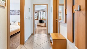 A hallway with a bed, a wooden bench, and a bathroom visible through an open door. - Apartment "Pramstaller Kron" with Mountain View, Wi-Fi, Terrace & Garden (St. Lorenzen)