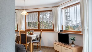 A room with a dining table, chairs, a TV on a wooden cabinet, and a window with curtains. - Apartment "Pramstaller Kron" with Mountain View, Wi-Fi, Terrace & Garden (St. Lorenzen)