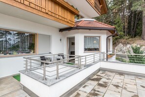 A modern house with a balcony, a wooden deck, and a stone patio.