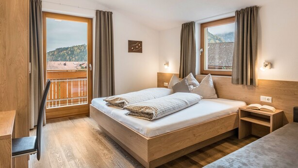 Ein Schlafzimmer mit einem Holzbett, einem Nachttisch, einem Stuhl und Blick auf einen Balkon.