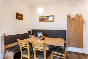 Un coin repas avec une table en bois, un banc noir rembourré et un saladier rempli de fruits.