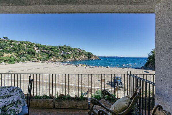 Un balcón con vista a la playa, un comedor con mobiliario exterior y un cielo azul despejado.