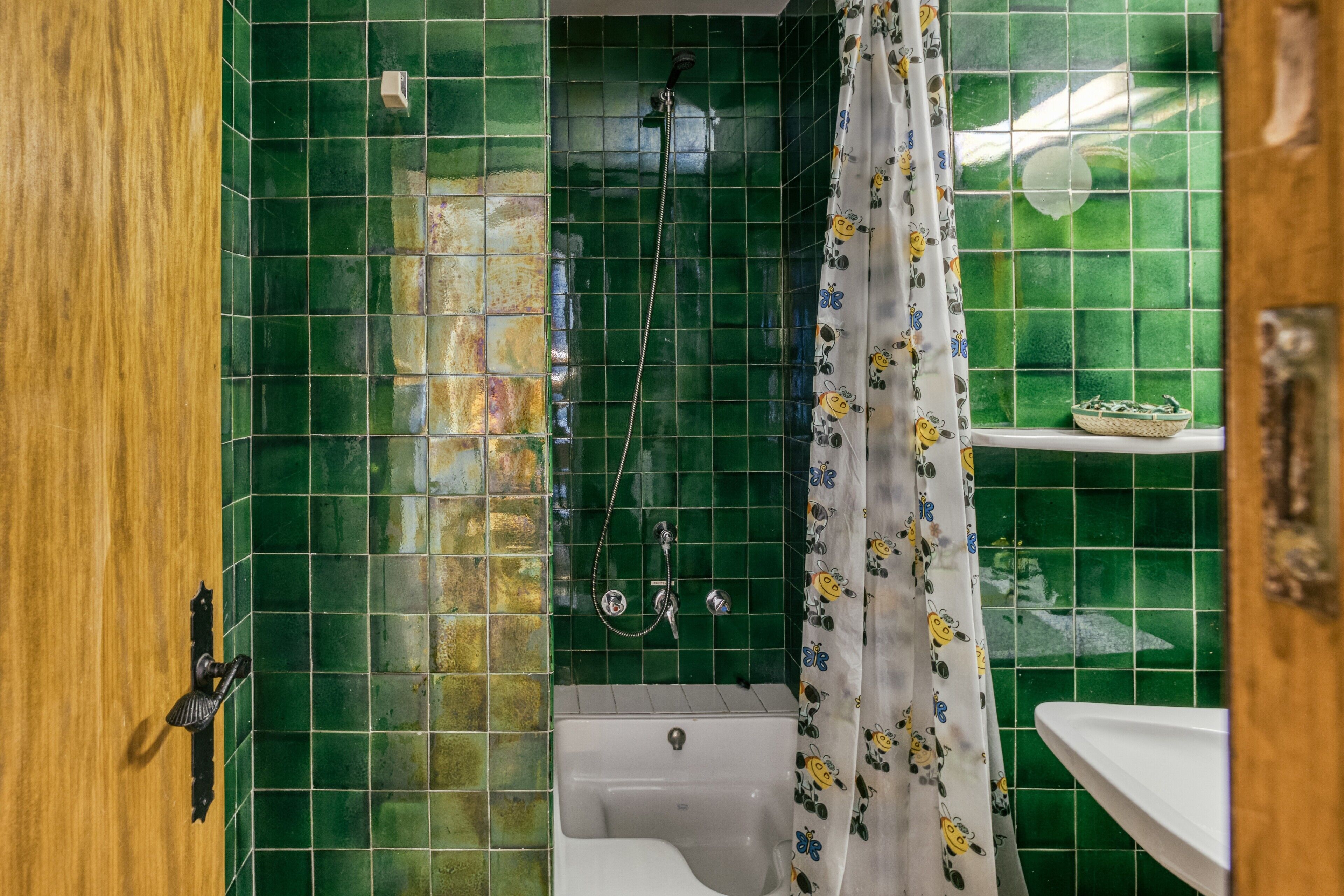 A bathroom with green tiles, a shower, a bathtub, a sink, and a door.