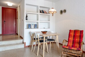 Ein Essbereich mit Tisch, Stühlen, einem Korbstuhl, einem Bücherregal und einer roten Tür.