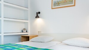 Un dormitorio con cama, almohadas blancas, colcha colorida, mesita de noche con radio y lámpara de pared.