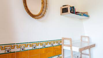 Een kamer met een witte muur, een spiegel met houten lijst, een plank met boeken, een betegelde achterwand en een houten stoel.