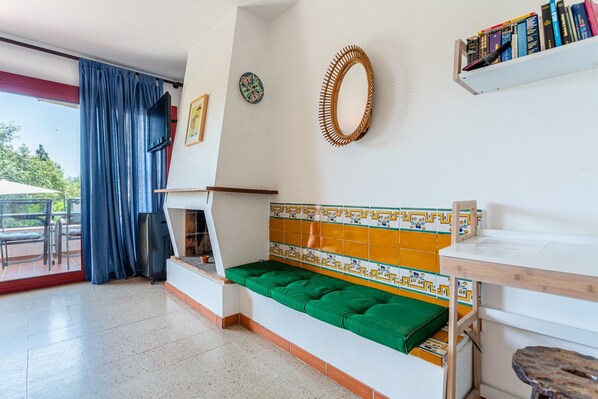 Una habitación con un banco acolchado verde, una pared de azulejos, una estantería de madera con libros y un televisor montado en la pared.