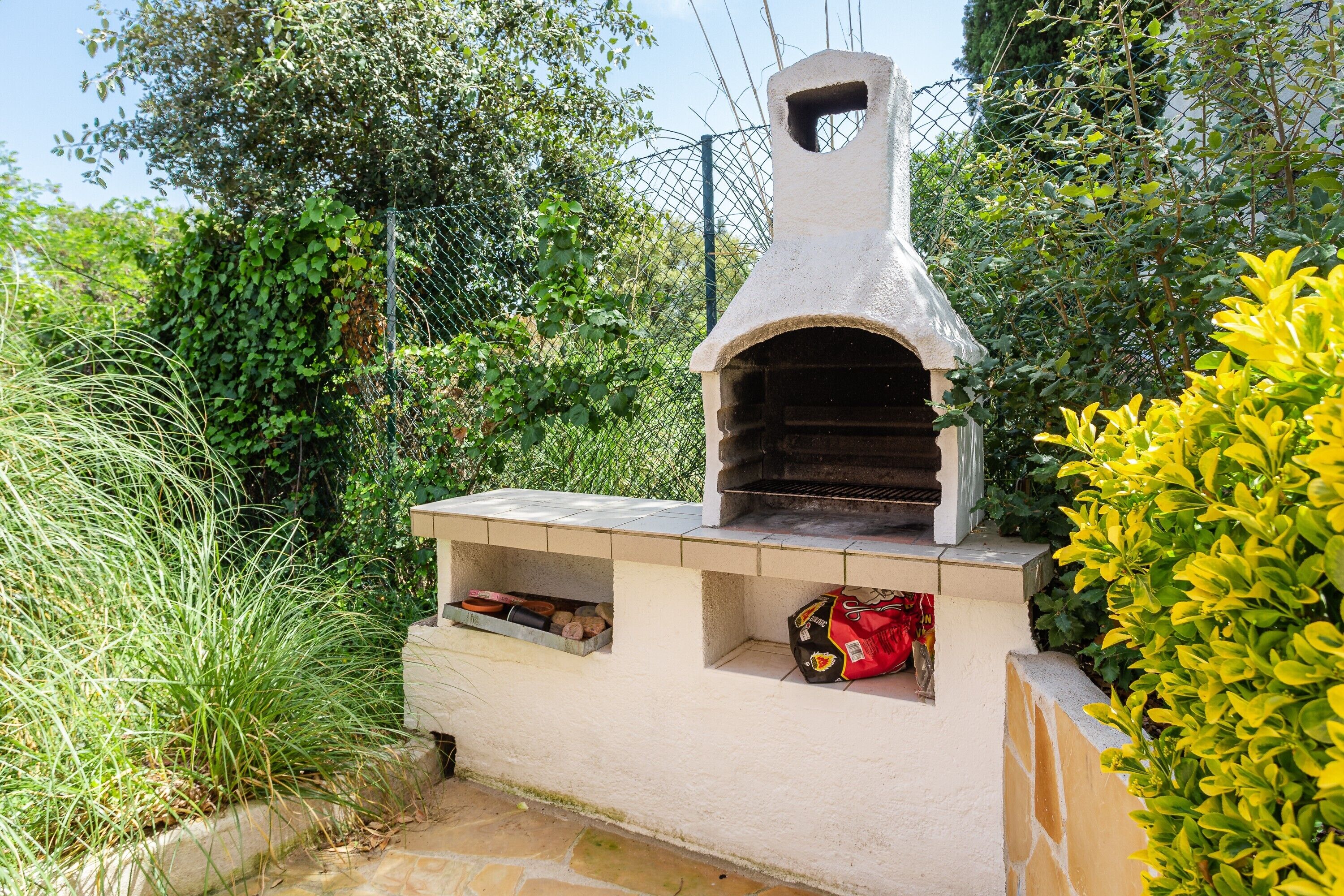 Un área de barbacoa al aire libre con horno de ladrillo, una pared de piedra, un hoyo para fuego y una bolsa de carbón.