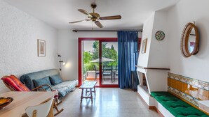 Un salón con sofá, una mesa de comedor, un ventilador de techo y vistas al exterior.