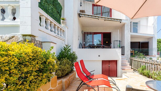 Un edificio de dos plantas con fachada de piedra, un balcón con mobiliario exterior y una escalera que conduce al nivel superior.